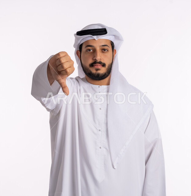 Feeling upset about something, the concept of rejection and failure, a close-up portrait of an Emirati Gulf Arab man wearing a kandora and ghutra, lowering his thumb with gestures of rejection and non-acceptance, elegance and attention to external appearance, white background.