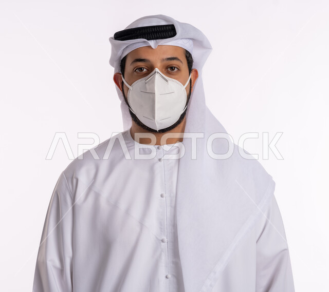 إتباع الإجراءات الوقائيه ضد الفايروسات، تجنب الملامسه السطحيه والحفاظ على المسافات، بورتريه مقرب لرجل عربي خليجي اماراتي يرتدي الكندوره والغتره البيضاء يضع القناع الطبي الوقائي للوقايه من فايروس كورونا، خلفيه بيضاء