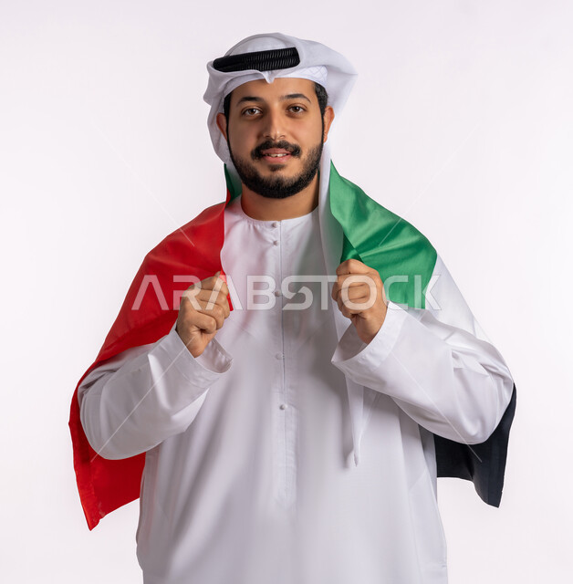 احياء ذكرى استقلال الإمارات، بورتريه لرجل عربي خليجي إماراتي يرتدي الكندورة والغترة البيضاء يقوم بحمل علم الإمارات العربية المتحدة على ظهره، الحب والانتماء للوطن، مفهوم الاعتزاز والفخر بإنجازات البلاد، هوية اليوم الوطني الاماراتي 51، الإحتفال باليوم الوطني الإماراتي، خلفية بيضاء