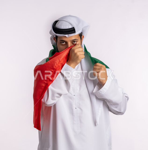 هوية اليوم الوطني الاماراتي 51، الإحتفال باليوم الوطني الإماراتي، يوم استقلال الإمارات، الاعتزاز والفخر بإنجازات البلاد، الحب والانتماء للوطن، بورتريه مقرب لرجل عربي خليجي إماراتي يرتدي الكندورة والغترة البيضاء يقوم بتقبيل علم الإمارات العربية المتحدة، خلفية بيضاء