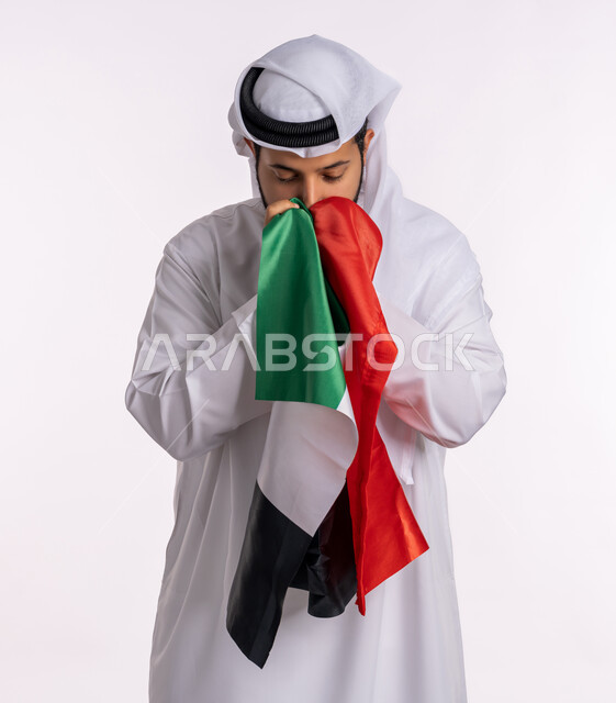 الإحتفال باليوم الوطني الإماراتي، هوية اليوم الوطني الإماراتي 51 ، يوم استقلال الإمارات، الاعتزاز والفخر بإنجازات البلاد، الحب والانتماء للوطن، بورتريه لرجل عربي خليجي إماراتي يرتدي الكندورة والغترة البيضاء يقوم بتقبيل علم الإمارات العربية المتحدة، خلفية بيضاء