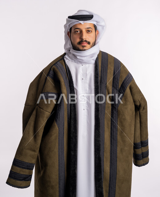 الوقوف باستقامة والنظر إلى الكاميرا بايماءات الثقة بالنفس، مفهوم الرجولة والاناقة، الاهتمام بالمظهر الخارجي، الملابس المناسبة لفصل الشتاء، الأجواء الشتوية الباردة، بورتريه لرجل عربي خليجي إماراتي يرتدي الفروة الغترة البيضاء، خلفية بيضاء