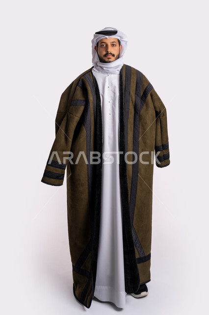 The concept of masculinity and elegance, standing upright and looking at the camera with gestures of self-confidence, taking care of the external appearance, appropriate clothes for the winter, cold winter weather, a portrait of an Arab Gulf Emirati man wearing a white ghutra, full body photo, white background.