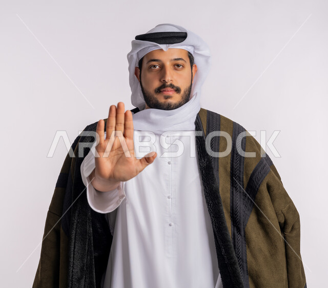 إيماءات الرفض والامتناع، طلب المنع والتوقف عن فعل شيء ما، بورتريه مقرب لرجل عربي خليجي إماراتي يرتدي الفروة والغترة ينظر إلى الكاميرا بتعابير الحزم والجدية، ارتداء الملابس المناسبة لفصل الشتاء، خلفية بيضاء