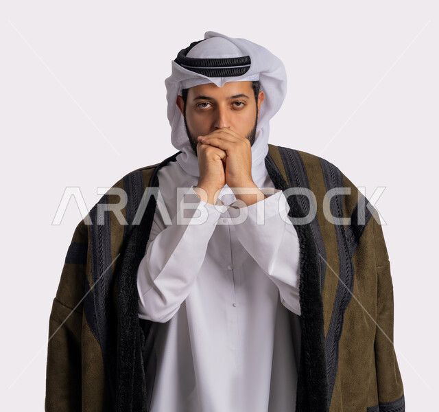 Facial and hand gestures indicating extreme cold, feeling of frost, chills and freezing, cold winter weather, close-up portrait of an Emirati Gulf Arab man wearing a white scalp and ghutra, warming his hands, wearing appropriate clothes for the winter, white background.
