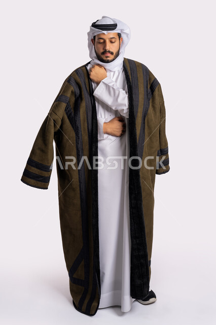 الشعور بالصقيع والقشعريرة والتجمد، إيماءات وجه ويدين تدل على البرد الشديد، الأجواء الشتوية الباردة، بورتريه لرجل عربي خليجي اماراتي يرتدي الفروة والغترة البيضاء، تعابير التعب والإرهاق، ارتداء الملابس المناسبة لفصل الشتاء، صورة لكامل الجسم، خلفية بيضاء