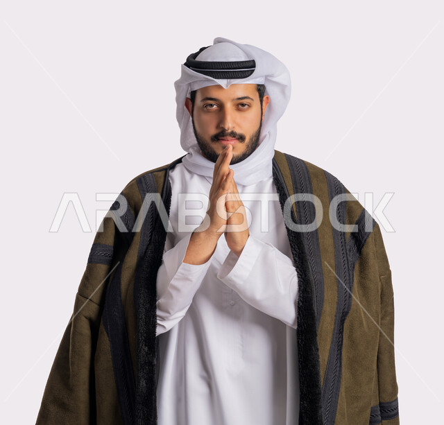 إيماءات وجه ويدين تدل على البرد الشديد، الشعور بالصقيع والقشعريرة والتجمد، الأجواء الشتوية الباردة، بورتريه مقرب لرجل عربي خليجي اماراتي يرتدي الفروة والغترة البيضاء يقوم بتدفئة يديه، ارتداء الملابس المناسبة لفصل الشتاء، خلفية بيضاء