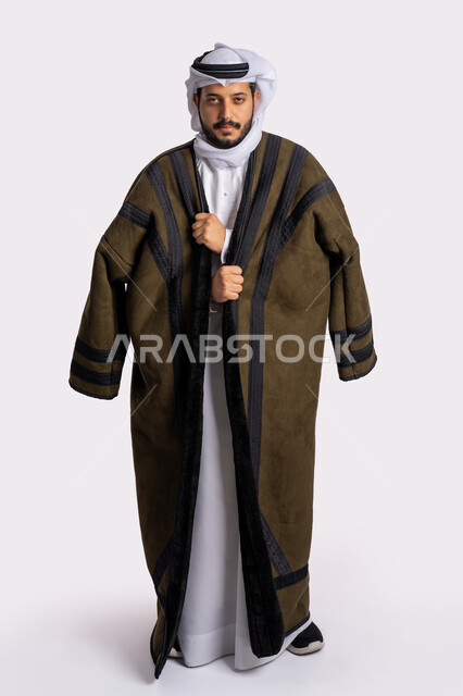 الشعور بالصقيع والقشعريرة والتجمد، إيماءات وجه ويدين تدل على البرد الشديد، الأجواء الشتوية الباردة، بورتريه لرجل عربي خليجي اماراتي يرتدي الفروة والغترة البيضاء ينظر غلى الكاميرا بتعابير التعب والإرهاق، صورة لكامل الجسم، خلفية بيضاء