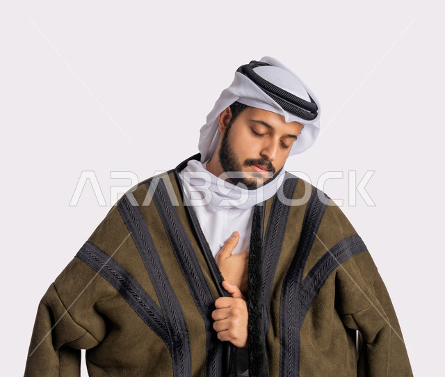 إيماءات وجه ويدين تدل على البرد الشديد، الأجواء الشتوية الباردة، الشعور بالصقيع والقشعريرة والتجمد، بورتريه لرجل عربي خليجي اماراتي يرتدي الفروة والغترة البيضاء يقوم بحني رأسه وإغماض عينيه بتعابير التعب والمرض، خلفية بيضاء