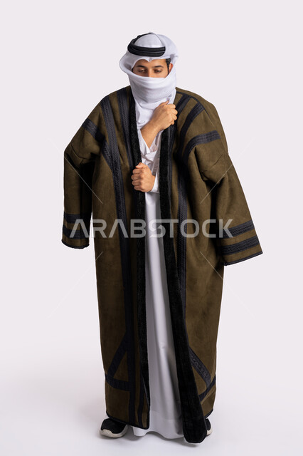 الأجواء الشتوية الباردة، إيماءات وجه ويدين تدل على البرد الشديد، الشعور بالصقيع والقشعريرة والتجمد، بورتريه لرجل عربي خليجي اماراتي يرتدي الفروة والغترة البيضاء يقوم بتغطية انفه وتدفئة يديه، صورة الجسم بالطول الكامل، خلفية بيضاء
