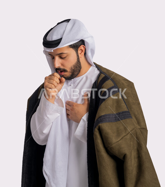 الحاجة لتلقي العلاج، الاصابة بفايروس كورونا كوفيد19، الاجواء الشتوية الباردة، الانفلونزا والتهاب الرئة، بورتريه مقرب من الجانب لرجل عربي خليجي اماراتي يرتدي الفروة والغترة البيضاء يعاني من السعال، الشعور بالمرض والكحة، خلفية بيضاء