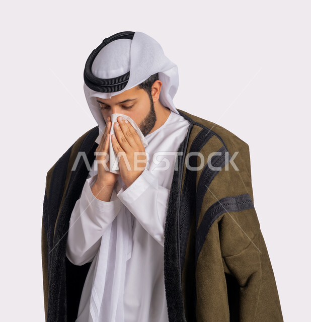 الشعور بالتعب والمرض، استعمال المناديل الورقية أثناء العطس، الإصابة بفايروس كورونا كوفيد19، بورتريه مقرب لرجل عربي خليجي اماراتي يرتدي الفروة والغترة البيضاء، الحاجة لتلقي العلاج، إيماءات وجه ويدين تدل على العطاس، خلفية بيضاء