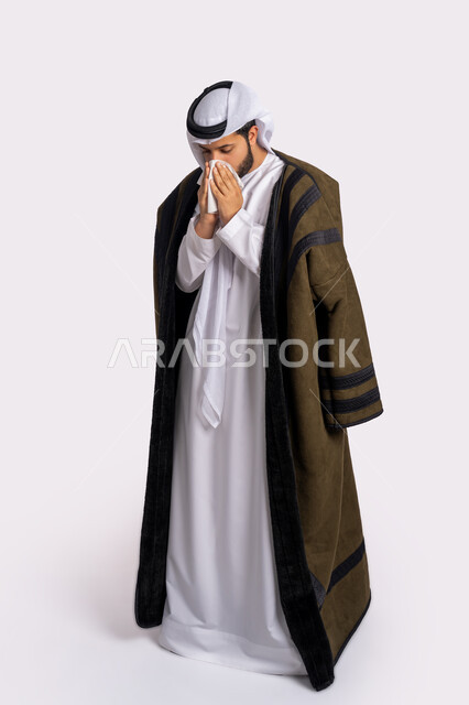 الإصابة بفايروس كورونا كوفيد19، الشعور بالتعب والمرض، استعمال المناديل الورقية أثناء العطس، بورتريه لرجل عربي خليجي اماراتي يرتدي الفروة والغترة البيضاء، الحاجة لتلقي العلاج، إيماءات وجه ويدين تدل على العطاس، صورة الجسم بالطول الكامل، خلفية بيضاء