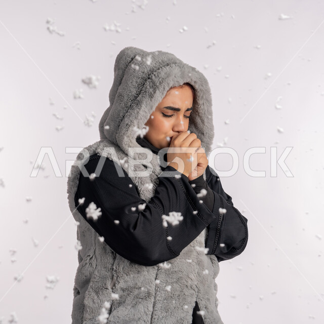 Season of snow, flu, lung inflammation, disease and coughing, cold winter atmosphere, portrait close to the side of an Emirati Gulf Arab woman wearing a winter coat suffering from coughing, a young Saudi woman with Virus Corona Kovid 19, gray background