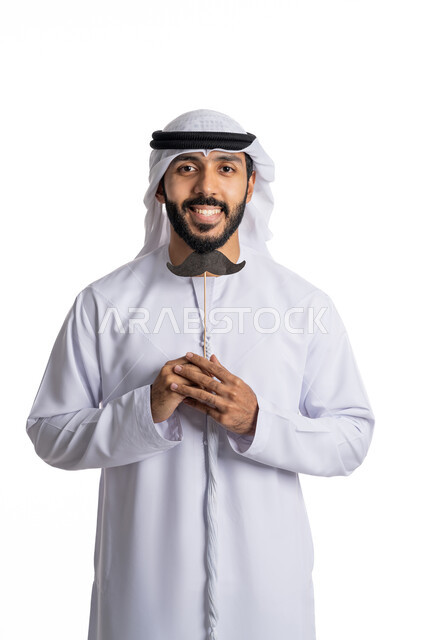 اليوم العالمي للرجال 19 نوفمبر ,  بورتريه مقرب لرجل عربي إماراتي خليجي يرتدي الكندورة والغترة البيضاء يحمل بيده قصاصة ورقية على شكل شارب, النظر إلى الكاميرا   الثقة والاعتزاز بالنفس ,  الاهتمام بصحة الذكور , خلفية بيضاء