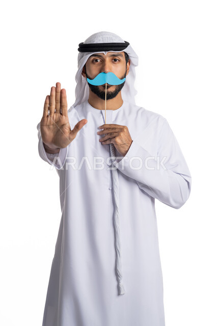 International signs of warning and caution, a portrait of an Arab Gulf Emirati man wearing a ghutra and a kandura, raising his hand to prevent getting too close to him and holding a piece of paper in the shape of a mustache, annual international events, the concept of caring for men, white background