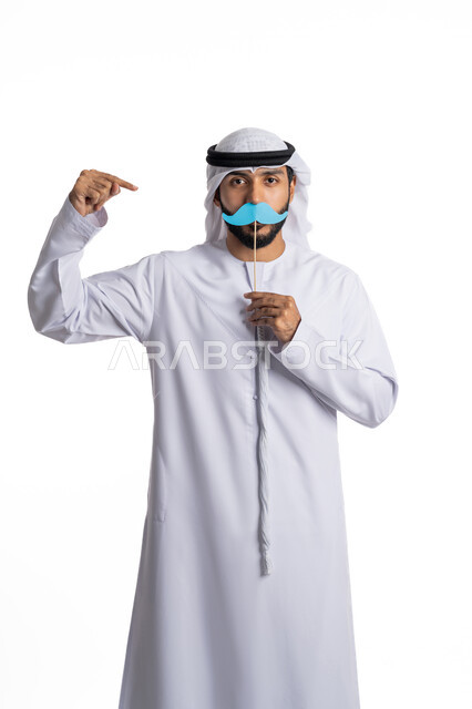 مناسبات عالمية سنوية، الاحتفال السنوي باليوم العالمي للرجل 19 نوفمبر، بورتريه لرجل عربي خليجي إماراتي يرتدي الكندورة والغترة ويحمل بيده قصاصة ورقية على شكل شارب، الوقوف باستقامة والنظر إلى الكاميرا والإشارة إلى القصاصة، مفهوم الاهتمام بالرجل، خلفية بيضاء