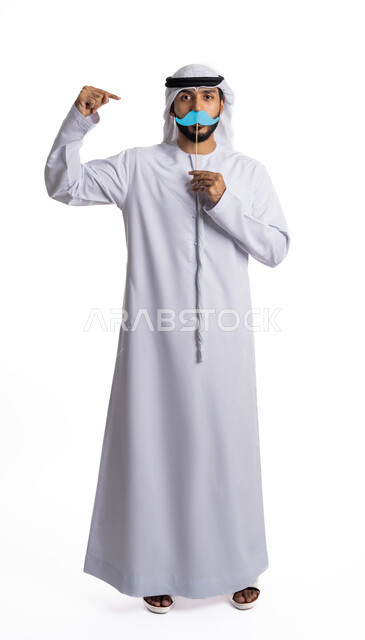 الاحتفال السنوي باليوم العالمي للرجل 19 نوفمبر، بورتريه لرجل عربي خليجي إماراتي يرتدي الكندورة والغترة ويحمل بيده قصاصة ورقية على شكل شارب، الوقوف باستقامة والنظر إلى الكاميرا والإشارة إلى القصاصة، مفهوم الاهتمام بالرجل، مناسبات عالمية سنوية، خلفية بيضاء