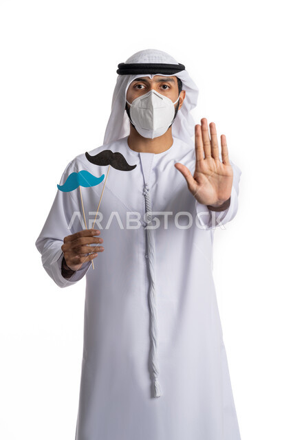 الالتزام بالاحترازات الوقائية ضد كوفيد 19(فايروس كورونا), بورتريه لشاب عربي خليجي إماراتي يرتدي الكندورة والغترة ويضع الكمامة للوقاية من فايروس كورونا ويحمل بيده قصاصات ورقية  باللون الأزرق والأسود على شكل شارب يرفع يده للأعلى بإيماءات التنبيه والتحذير  لمنع الاقتراب، الاهتمام بالصحة العامة, خلفية بيضاء