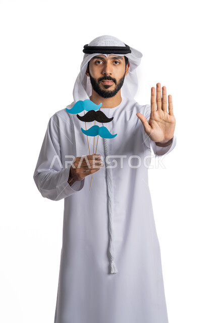 رفع اليد بايماءات التحذير والتنبيه، الاحتفال باليوم العالمي للرجل 19 نوفمبر، طلب التوقف عن فعل شيء ما، الإهتمام بصحة الذكور، بورتريه لشاب عربي خليجي إماراتي يرتدي الكندورة والغترة يحمل عود خشبي عليه قصاصات ورقية على شكل شارب، خلفية بيضاء