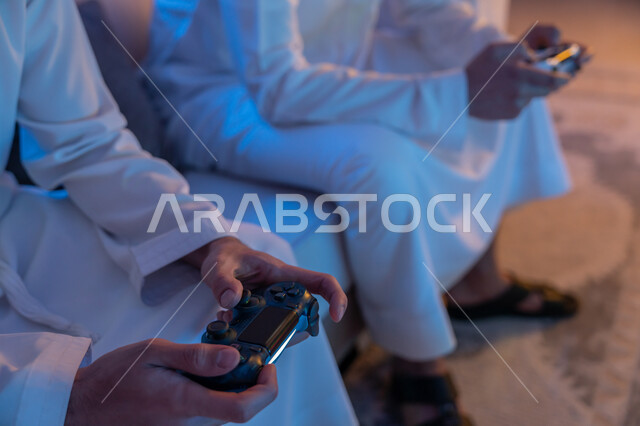 الاستمتاع بقضاء الوقت الممتع برفقة الأصدقاء, المشاركة والمنافسة بالألعاب التقنية الحديثة والمتطورة, رجلان عربيان خليجيان اماراتيان يرتديان الكندورة الاماراتية يمسكان عصا التحكم, العالم الرقمي الترفيهي, المتعة والتسلية بالفيديو جيمز