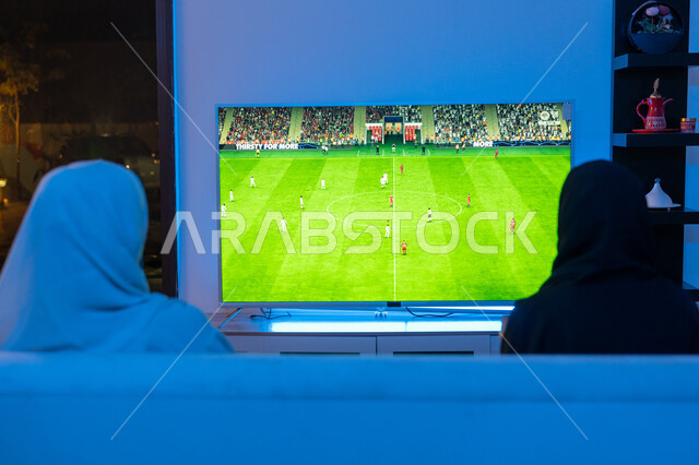 التسلية وقضاء الوقت الممتع برفقة الأصدقاء, المشاركة والمنافسة بالألعاب التقنية الحديثة والمتطورة, صورة من الخلف لشابتين سعوديتين تقومان باللعب الفيديو جيمز, سيدتان عربيتان خليجيتان اماراتيتان ترتديان العباءة والحجاب تجلسان باندماج وتركيز