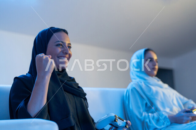 Integration, interaction and enthusiasm in the modern and advanced electronic digital world, participation in video games, a close-up of two Saudi young women holding the joystick with concentration, two Arab Gulf and Emirati women competing to achieve victory and triumph, fun and entertaining entertainment experiences