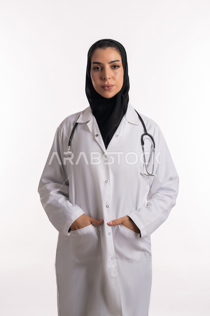 مفهوم الأنوثة والنعومة، الأناقة والاهتمام بالمظهر الخارجي، طبيبة عربية خليجية سعودية محجبة  ترتدي المعطف الطبي تضع السماعات الطبية، بورتريه مقرب لشابة إماراتية تنظر إلى الكاميرا بايماءات الثقة بالنفس، تقديم الاستشارات الطبية والخدمات الصحية، خلفية بيضاء
