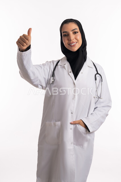 Raising a hand with gestures of quality and admiration for something, a Saudi Arabian Gulf doctor wearing a medical coat pointing with a thumb upward, a close-up portrait of a young Emirati woman looking at the camera, providing medical consultations and health services, satisfaction and acceptance of the quality of medical services, white background