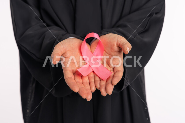 تحدي الأمراض الخبيثة، رمز الحملة العالمية، بورتريه مقرب لأيدي إمرأة عربية خليجية إماراتية ترتدي العباية تحمل الشريط الوردي بين يديها، حملة توعوية للكشف المبكر عن سرطان الثدي، اليوم العالمي للتوعية والكشف المبكر، خلفية بيضاء