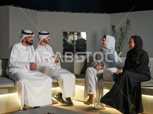 تبادل الأحاديث الشيقة بايماءات البهجة والسرور، أجواء ليلية هادئة، مجموعة من الشباب العرب الخليجيين الإماراتيين يرتدون الكندورة والغترة يجلسون في شرفة منزل، شابتان محجبتان ترتديان العباية يقومون بقضاء أوقات ممتعة مع الأصدقاء، الديكورات الخارجية الراقية