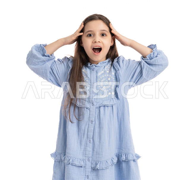 الذهول و الصدمة والتفاجؤ من شيئ ما, بورتريه مقرب لفتاة عربية امارتية خليجية بتعابير وجه ويدين تدل على الدهشه و التعجب, بنت سعودية ترتدي الفستان وترفع يديها على رأسها بإيماءات الفرح والسعادة، خلفية بيضاء