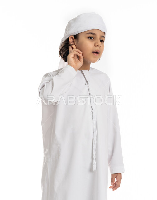 محاولة التجسس والتنصت, بورتريه مقرب لولد عربي اماراتي خليجي يرتدي العمامة والكندورة ويضع يديه خلف اذنيه بإيماءات تدل على الإنصات, حسن الإستماع و التركيز على الكلام, فتى سعودي يقوم بسماع الأسرار والمحادثات، خلفية بيضاء