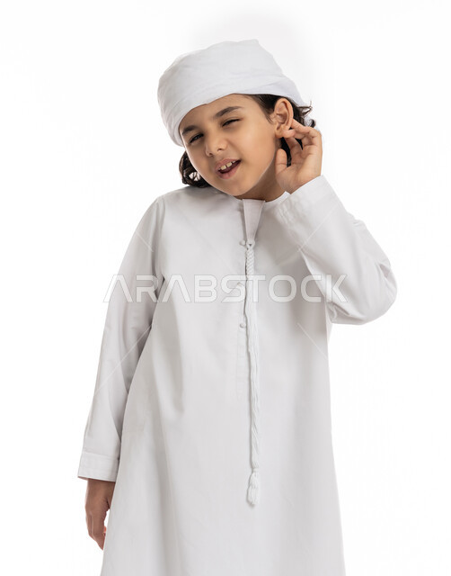 محاولة التجسس والتنصت, بورتريه مقرب لولد عربي اماراتي خليجي يرتدي العمامة والكندورة ويضع يديه خلف اذنيه بإيماءات تدل على الإنصات, حسن الإستماع و التركيز على الكلام, فتى سعودي يقوم بسماع الأسرار والمحادثات، خلفية بيضاء