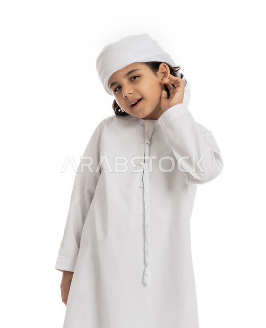محاولة التجسس والتنصت, بورتريه مقرب لولد عربي اماراتي خليجي يرتدي العمامة والكندورة ويضع يديه خلف اذنيه بإيماءات تدل على الإنصات, حسن الإستماع و التركيز على الكلام, فتى سعودي يقوم بسماع الأسرار والمحادثات، خلفية بيضاء