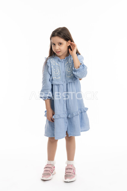 سماع الأحاديث و النقاشات، محاولة التجسس والتنصت, إيماءات الإنصات وكشف الاسرار, بورتريه لفتاة عربية اماراتية خليجية ترتدي الفستان تضع يديها خلف اذنيها, بنت سعودية تقوم بالإستماع و التركيز على الكلام, صورة الجسم بالكامل، خلفية بيضاء