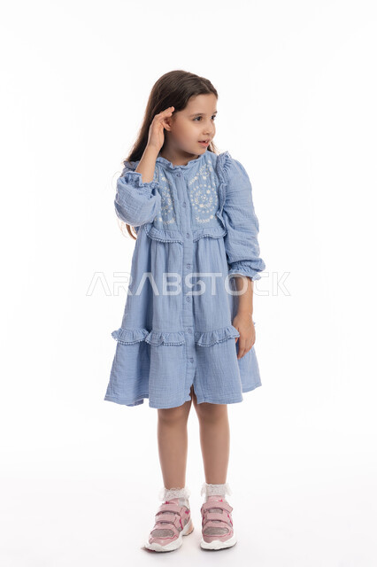 سماع الأحاديث و النقاشات، محاولة التجسس والتنصت, إيماءات الإنصات وكشف الاسرار, بورتريه لفتاة عربية اماراتية خليجية ترتدي الفستان تضع يديها خلف اذنيها, بنت سعودية تقوم بالإستماع و التركيز على الكلام, صورة الجسم بالكامل، خلفية بيضاء