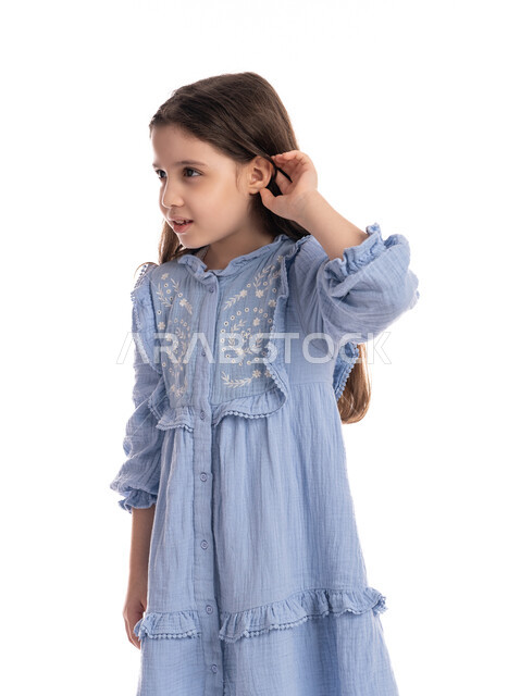إيماءات الإنصات وكشف الاسرار, سماع الأحاديث و النقاشات، محاولة التجسس والتنصت, بورتريه مقرب لفتاة عربية اماراتية خليجية ترتدي الفستان تضع يديها خلف اذنيها, بنت سعودية تقوم بالإستماع و التركيز على الكلام, خلفية بيضاء