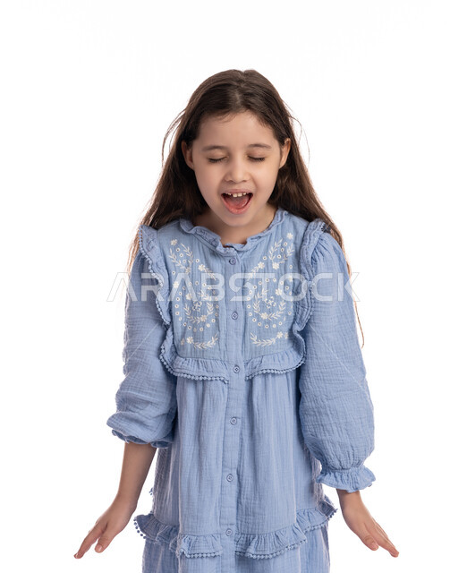 الصراخ والغضب من شيء ما, فتاة سعودية تقف بايماءات يدين ووجه تدل على الضجر و الاستياء وعدم الرضا, بورتريه مقرب لبنت عربية اماراتية خليجية ترتدي الفستان ترفع يديها للاعلى بتعابير العصبية, خلفية بيضاء