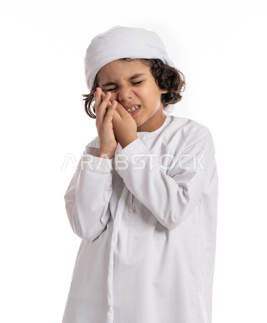 التهاب اللثه وتسوس الأَضراس, الاحتياج الى زيارة طبيب الأسنان، بورتريه مقرب لولد عربي اماراتي خليجي يرتدي الكندورة و العمامة يضع يده على خده بإيماءات تدل على ألم الأسنان, فتى سعودي يعاني من التعب والإرهاق والحاجة لطلب العلاج والمساعده, خلفية بيضاء