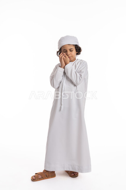 الاحتياج الى زيارة طبيب الأسنان، التهاب اللثه وتسوس الأَضراس, بورتريه لولد عربي اماراتي خليجي يرتدي الكندورة و العمامة يضع يده على خده بإيماءات تدل على ألم الأسنان, فتى سعودي يعاني من التعب والإرهاق والحاجة لطلب العلاج والمساعده, صورة الجسم بالكامل، خلفية بيضاء