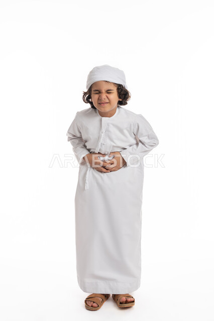 الإحساس بالمغص و التعب والإرهاق, طلب المساعده للذهاب الى الطبيب، فتى سعودي يعاني من عسر الهضم وحرقة في المعدة، بورتريه لولد عربي اماراتي خليجي يرتدي الكندورة والعمامة يضع يديه على معدته بإيماءات الشعور بألم في البطن, صورة الجسم بالكامل، خلفية بيضاء