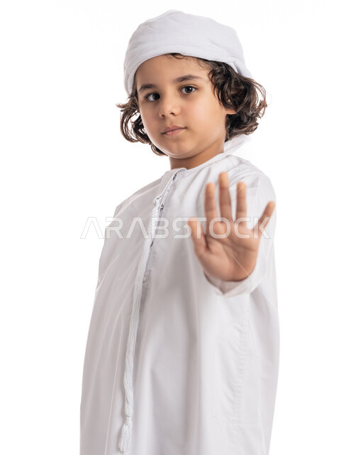 الشعور بالإنزعاج و الرفض والإمتناع، الصمت التوقف عن الكلام، فتى سعودي يقف بإيماءات يدين تدل على الأمر بالتوقف عن فعل شيء ما و النهي عنه، بورتريه لولد عربي اماراتي خليجي يرتدي الكندورة والعمامة الاماراتية ويرفع كفه للأعلى, خلفية بيضاء