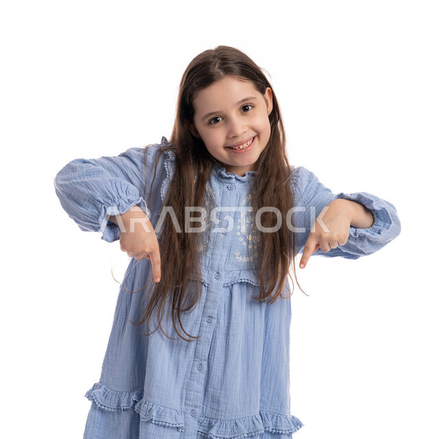 تحديد هذا المكان (هنا), إيماءات يدين تشير الى موقع معين, بورتريه مقرب لفتاة عربية اماراتية خليجية تشير بأصابعها إلى الاسفل, بنت سعودية مبتسمة ترتدي الفستان تقوم في توثيق هذه اللحظه (الآن)، خلفية بيضاء