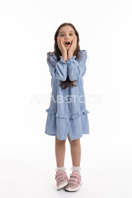 الذهول و الصدمة والتفاجؤ من شيئ ما, بورتريه لفتاة عربية امارتية خليجية بحركات وجه ويدين تدل على الدهشه والتعجب, بنت سعودية ترتدي الفستان وترفع يديها على وجهها بإيماءات الفرح والسعادة، صورة الجسم بالطول الكامل، خلفية بيضاء