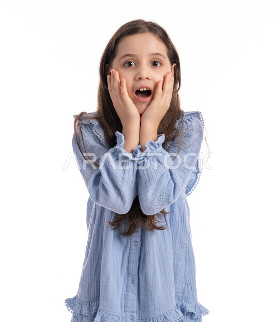 Shock, astonishment and surprise at something, a close-up portrait of an Arab Emirati Gulf girl with facial and hand movements indicating astonishment and wonder, a Saudi girl wearing a dress and raising her hands to her face with gestures of joy and happiness, white background.