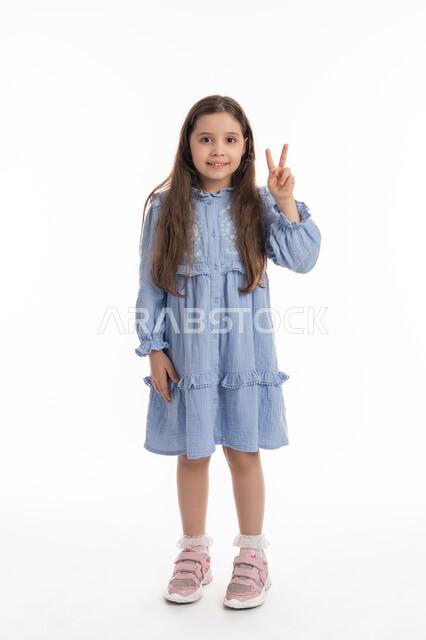 ايماءات وجه ويدين تدل على الإنتصار, الإعجاب والرضا, بنت سعودية ترتدي الفستان تشعر بالسعاده والفرح، علامة السلام والقوه, بورتريه لفتاة عربيه اماراتية خليجية ترفع يدها الى الاعلى بعلامة الفوز والكسب، صورة الجسم بالكامل، خلفية بيضاء