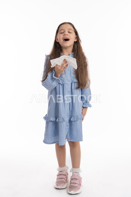 استخدام المناديل الورقيه للعطس، الشعور بالمرض و الزكام, الحاجة الى العلاج والدواء، فتاة سعودية ترتدي الفستان تشعر بالتعب و الارهاق، بورتريه لفتاة عربيه اماراتية خليجيه بإيماءات وجه ويدين تدل على العطاس, صورة الجسم بالكامل، خلفية بيضاء