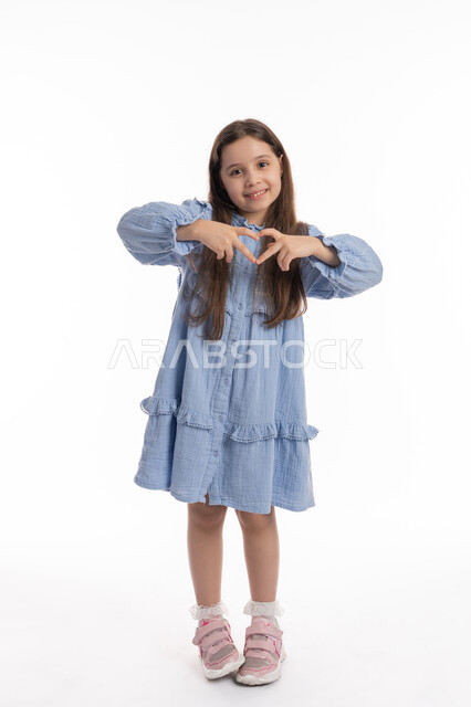 إيماءات وتعابير الشعور بالحب، التعبير عن المشاعر الإيجابية، السعاده والطمأنينه والمحبه, بورتريه لبنت عربية اماراتية خليجية ترتدي الفستان ترفع يديها بشكل قلب, فتاة سعودية تقوم بالاحتفال بعيد الحب (الفالنتاين)، صورة الجسم بالكامل، خلفية بيضاء