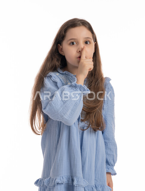 الأمر بالصمت والاستماع والتوقف عن الكلام، بورتريه مقرب لفتاة عربية خليجية اماراتية ترتدي الفستان ترفع اصبعها الى فمها, بنت سعودية تقف بإيماءات يدين تدل على طلب الهدوء و عدم الإزعاج, خلفية بيضاء
